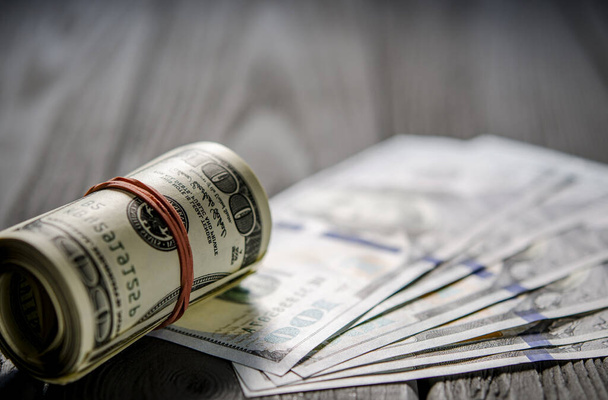 Толстый рулон банкнот за сто долларов, завязанный красной резинкой, лежит на бакенбарде стодолларовых купюр
 - Фото, изображение