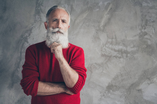 Photo of attractive white haired aged guy holding hand chin look clever eyes minded wear red knitted pullover hipster santa clothes isolated grey color concrete wall background - Φωτογραφία, εικόνα