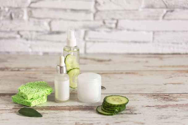 Bottles of homemade cucumber natural cosmetic with green cucumber slices and cotton-pads on wooden background. - Photo, Image
