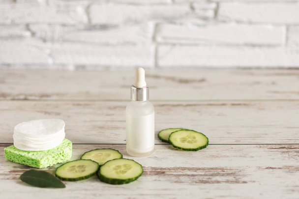 Bottle of homemade facial cucumber organic serum with green cucumber slices and cotton-pads on wooden background. - Photo, Image