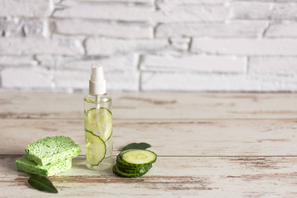Homemade refreshing facial cucumber toner in bottle with slices of green cucumber and cotton-pads on white wooden background. - Photo, Image
