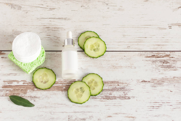 Bottle of homemade facial cucumber organic serum with green cucumber slices and cotton-pads on wooden background. - Photo, Image
