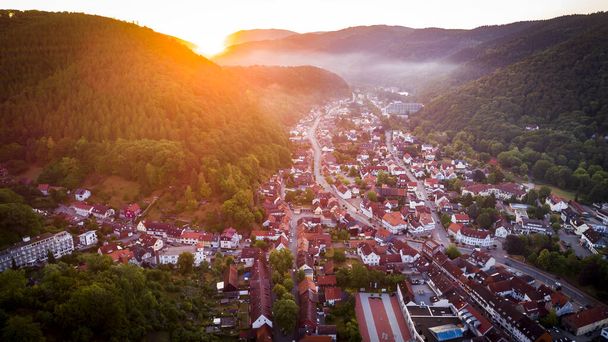 Letecký dron pohled z ptačí perspektivy fotografie evropské vesnice střední Evropy s červenými střechami a útulnými ulicemi, nádhernými přírodními ranními slunečními paprsky a mlhou v údolí - Fotografie, Obrázek