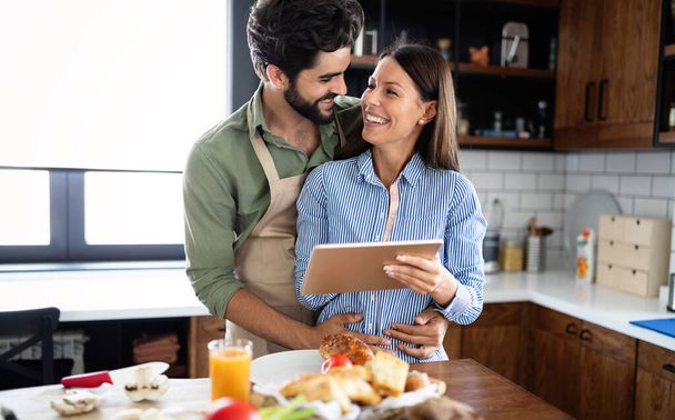 Happy young couple cooking together in their kitchen - Foto, Bild