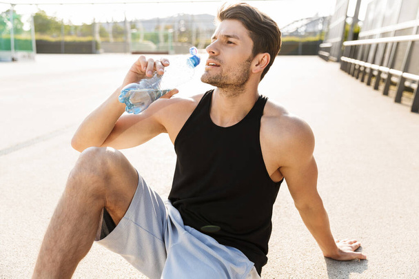 Portrait of handsome man drinking water while sitting on sports  - 写真・画像