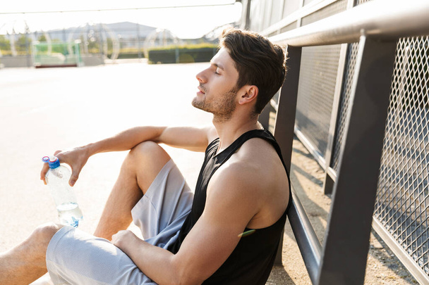 Portrait of relaxed man drinking water while sitting on sports g - Foto, immagini
