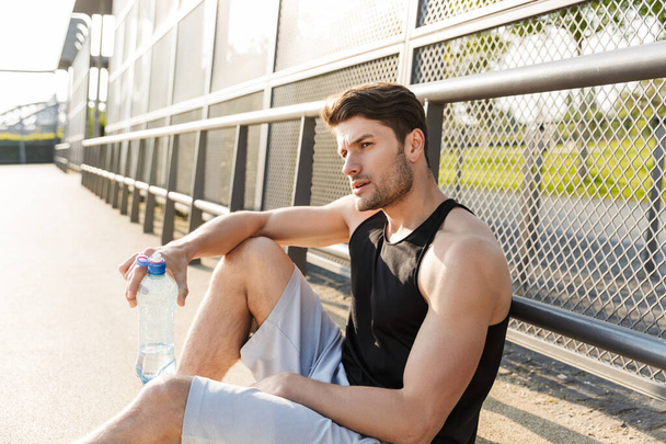 Portrait of attractive man drinking water while sitting on sport - Valokuva, kuva