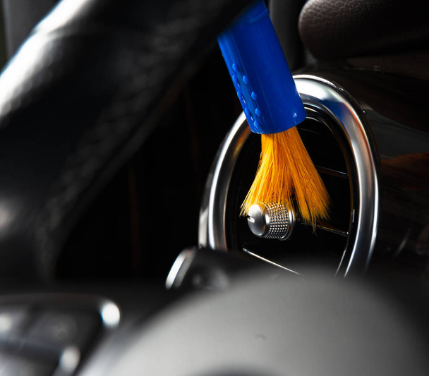 Harja puhdistaa pölyä auton sisustus yksityiskohtia, ohjauspaneeli kojelautaan. Mies puhdistaa autoa liinalla ja harjalla. Yksityiskohtia autosta. Työläisten siivous. Harjaa ja puhdistus ratkaisu puhdistaa
 - Valokuva, kuva