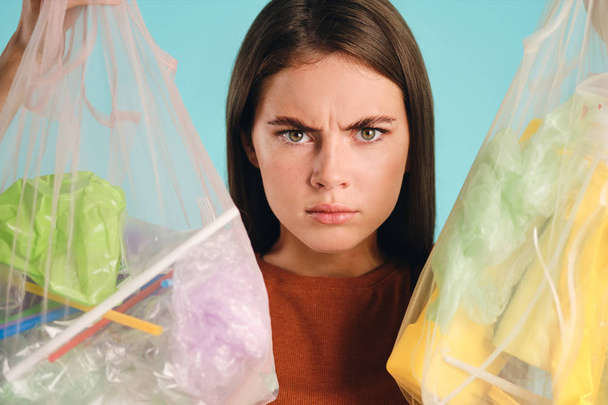 Zblízka naštvaný dívka drží eko tašky s plastovým odpadem a zuřivě se dívá do kamery přes barevné pozadí - Fotografie, Obrázek