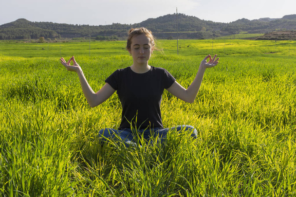 Mujer de pelo rojo caucásica joven, con el pelo largo y pecas, sentado en la hierba en una posición de yoga. mindfulness, meditación y escena relajante
 - Foto, imagen