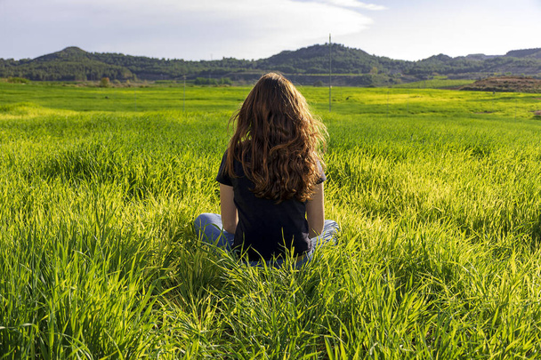 Young caucasian red-haired woman, with long hair and freckles, sitting on the grass in a yoga position. mindfulness, meditation and relaxing scene - 写真・画像
