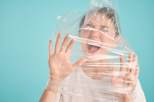 Afraid emotional girl scared screaming choking in plastic bag over colorful background  - Photo, Image