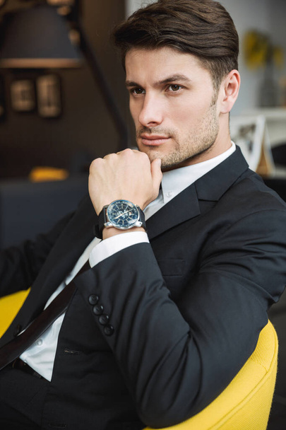 Portrait of brunette young businessman wearing wristwatch sittin - Fotó, kép