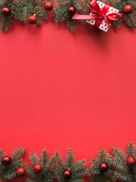 Χριστουγεννιάτικο πλαίσιο με κλαδιά ελάτης, κόκκινες μπάλες σε κόκκινο φόντο. Χώρος για κείμενο, θέα από ψηλά, επίπεδη lay. - Φωτογραφία, εικόνα