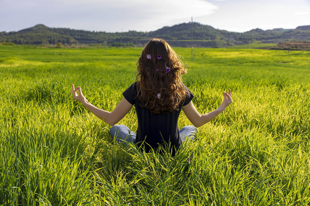 junge kaukasische rothaarige Frau, mit langen Haaren und Sommersprossen, die auf dem Gras in einer Yogaposition sitzt. Achtsamkeit, Meditation und entspannende Szene - Foto, Bild