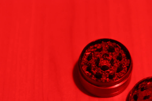 Ground medical marijuana close-up in a grinder. Preparing for smoking. Top view of accessories for drug use in red light - 写真・画像