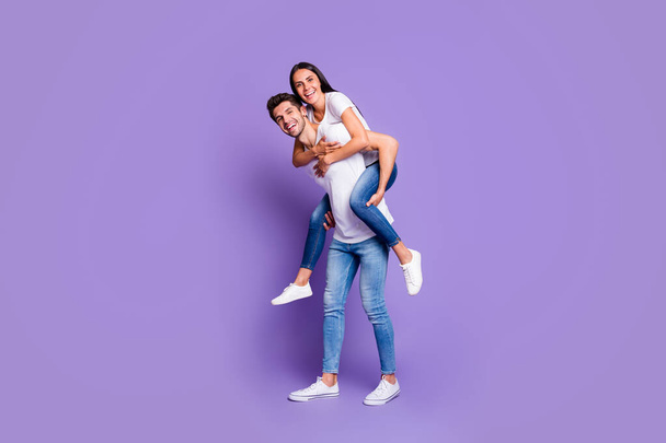 Turned full length body size photo of cute couple of two beloved people piggyback in white t-shirt smiling toothily with man carrying his woman isolated violet pastel color background - Photo, Image