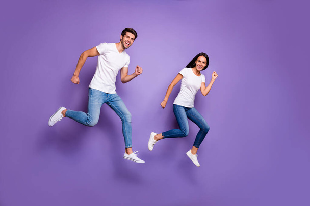 Turned full length body size photo of cute pretty nice couple of two people running jumping for sales in t-shirt white jeans denim footwear isolated violet pastel color background - Foto, Bild