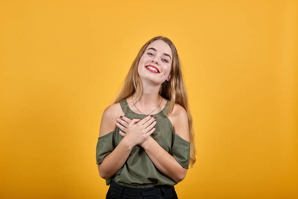 Retrato de una joven sonriente con camisa casual cogida de la mano en el pecho, el corazón
 - Foto, Imagen