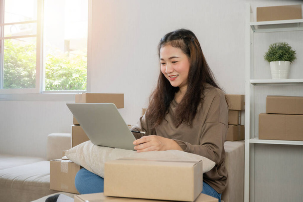 Young entrepreneur, sitting on the sofa and working at home. Checking orders from customers by laptop and writing customer address deliver shipment online sales. Concept of small business owner. - Foto, afbeelding