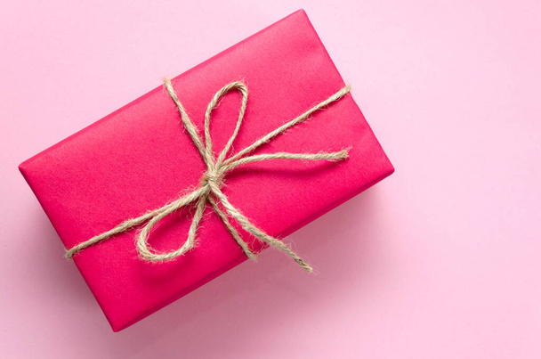 Roze geschenkdoos met bindgaren op een lichtroze achtergrond. Vakantie concept. Sterf huidig idee. Plat gelegd. Kopieerruimte - Foto, afbeelding