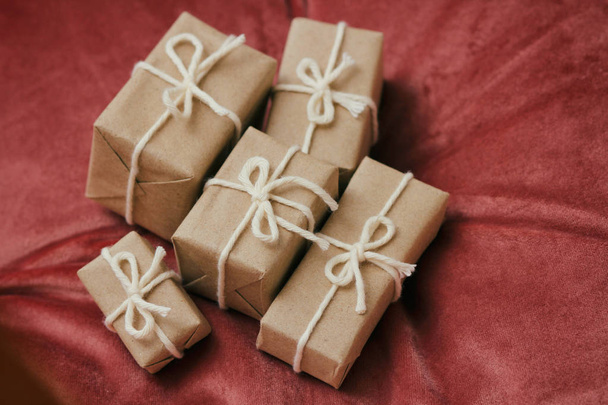 Presents for a Christmas. Gift boxes wrapped in craft paper and tie white string. Red velvet cloth background. Holiday mood. - Zdjęcie, obraz