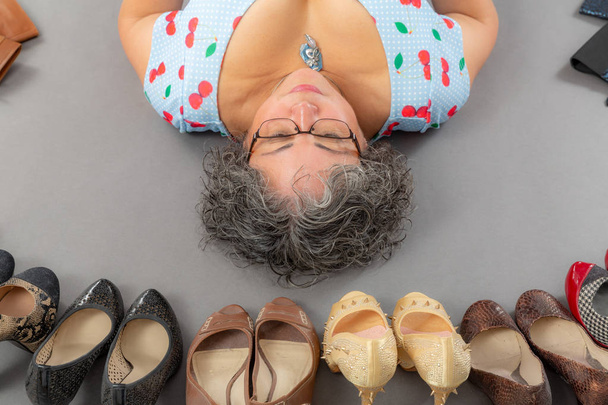 Dojrzała kobieta leżąca na podłodze otoczona różnymi butami - Zdjęcie, obraz