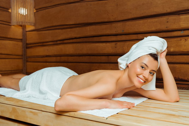 attractive and smiling woman in towels lying in sauna  - Foto, immagini