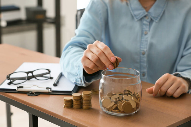 Een vrouw die munten in een pot op tafel doet. Begrip "geldbesparing" - Foto, afbeelding