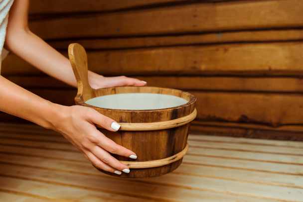 cropped view of woman holding wooden washtub in sauna  - Foto, Imagen
