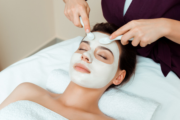 cropped view of cosmetologist applying face mask on attractive woman in spa  - Fotó, kép