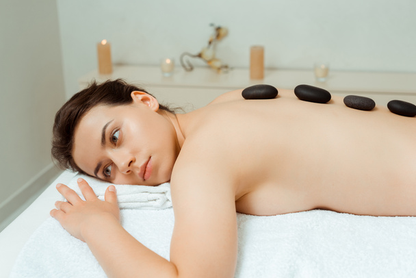 aantrekkelijke vrouw met hete stenen op de rug liggend op massagetafel in spa  - Foto, afbeelding