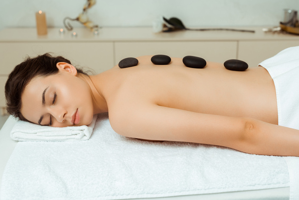 mulher atraente com pedras quentes nas costas deitado na mesa de massagem no spa
  - Foto, Imagem