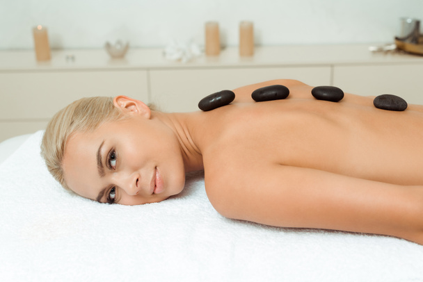femme souriante avec des pierres chaudes sur le dos couché sur la table de massage dans le spa
  - Photo, image