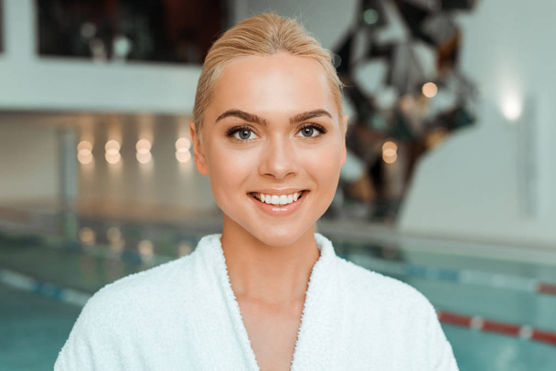 attractive and smiling woman in white bathrobe looking at camera in spa  - Фото, изображение