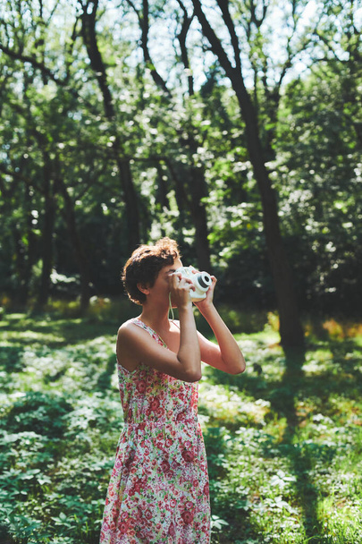 Aktiivinen tyttö ottaa valokuvan instant kamera aurinkoisessa metsässä
 - Valokuva, kuva