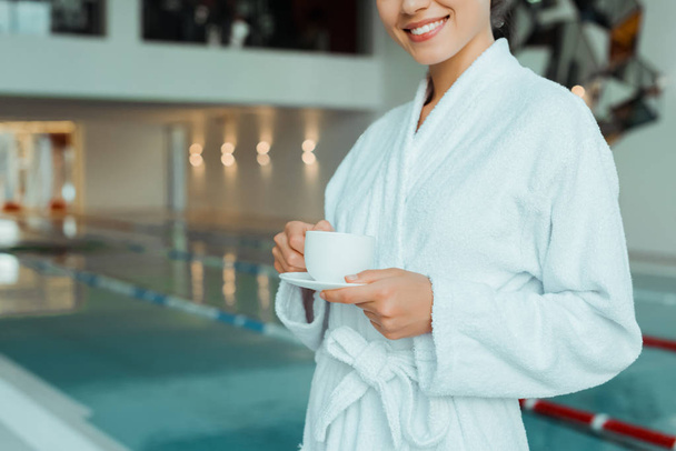 vue recadrée d'une femme souriante en peignoir blanc tenant une tasse de café dans un spa
  - Photo, image