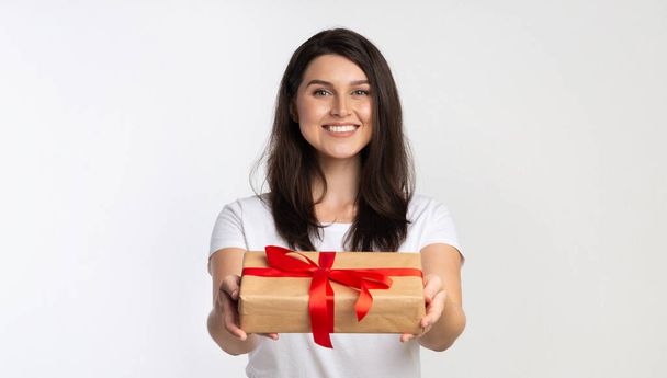 Garota oferecendo embrulhado caixa de presente para câmera em pé, fundo branco
 - Foto, Imagem