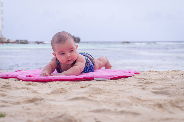 Dziecko na plaży leżące na piaskowej różowej macie - Zdjęcie, obraz