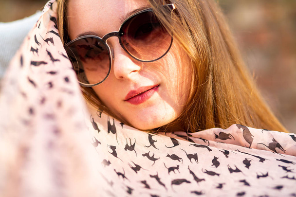 Autumn model. Young pretty white caucasian teenage girl with problem skin in sunglasses on the street in the autumn on sunny day. Close up. - Fotó, kép