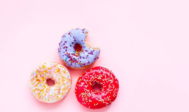 Gebissene farbige Donuts mit bunten Streuseln auf rosa Hintergrund. Nahaufnahme - Foto, Bild
