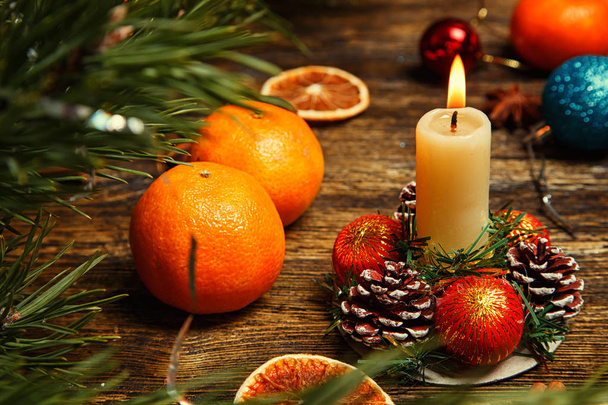 Christmas decoration with the burning candle, tangerines, pine cones and balls on a wooden table - Photo, image