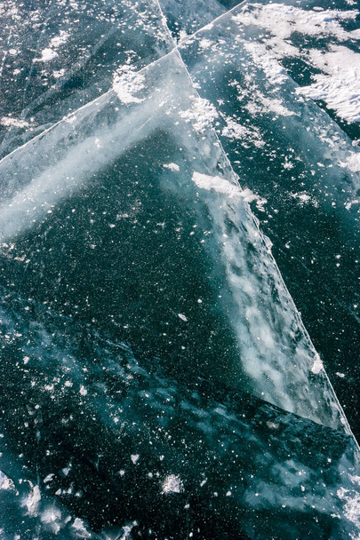 das Eis des Baikalsees mit Schnee mit tiefen Rissen gepudert. dicke Risse im Eis. vertikale Orientierung. - Foto, Bild