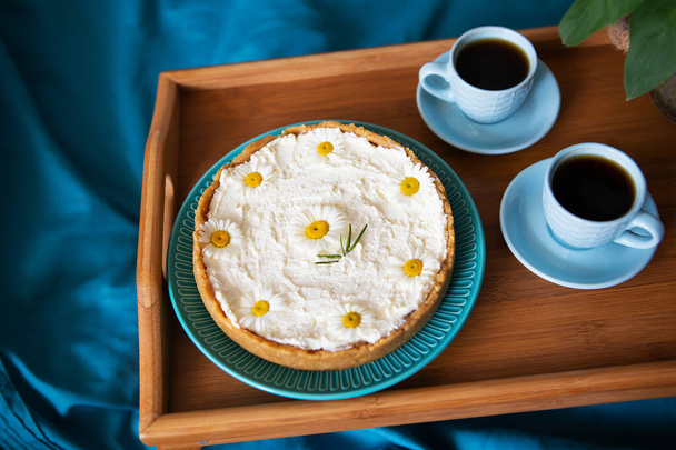 A cup of coffee and cream cheesecake stand on a wooden tray in bed. - Photo, Image