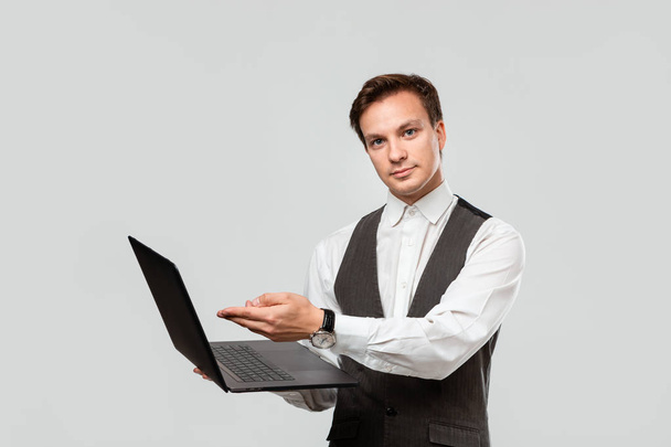 Menedżer trzymający laptopa i wskazujący ekran patrzący na odizolowaną kamerę na szarym tle - Zdjęcie, obraz