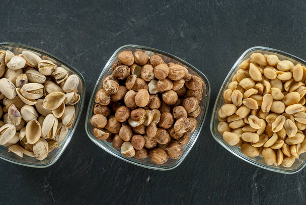 misky s různými ořechy jako lískových oříšků pistácie a arašídy na černé břidlice zdravý život koncept - Fotografie, Obrázek