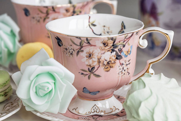 Чашки розового чая с цветочным орнаментом и сладости из макарон
 - Фото, изображение