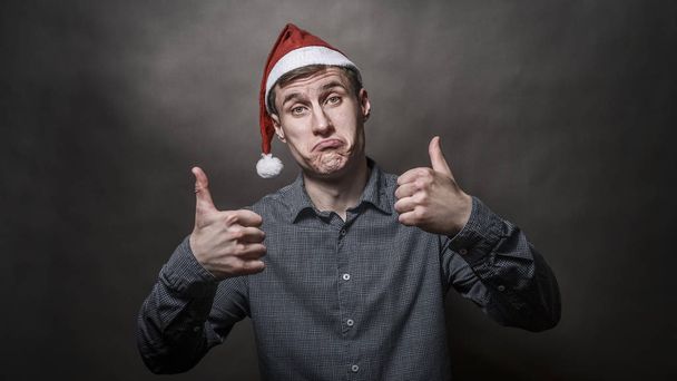Young handsome man dressed in a Santa Claus hat on a gray backgr - Foto, Bild