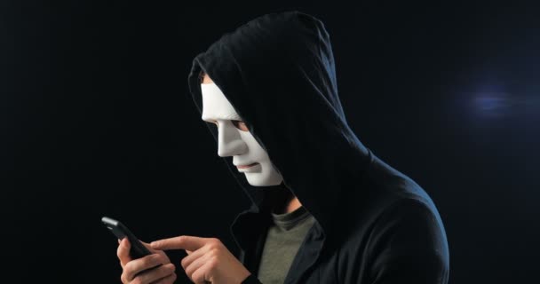 Anonymní maskovaný podvodník v kapuci požaduje výkupné za vydírání pomocí chytrého telefonu. Maskovaný trestný čin zastrašuje oběť pomocí hrozeb prostřednictvím Sms pomocí mobilního telefonu. - Záběry, video