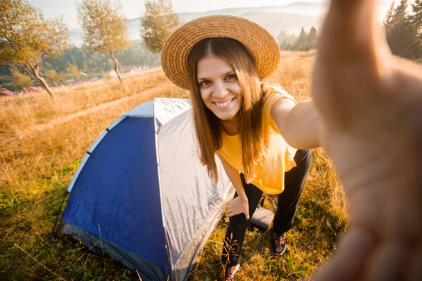 Mulher feliz em chapéu tirar selfie com câmera depois de acordar na tenda na manhã de outono
 - Foto, Imagem
